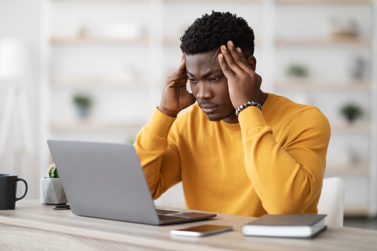 Stressed african american manager working on laptop, touching head