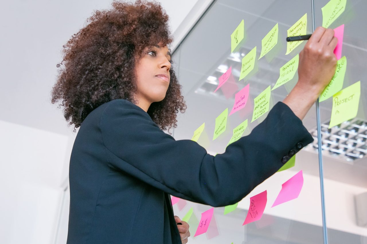 successful-pretty-businesswoman-writing-sticker-with-marker-thoughtful-confident-curly-female-manager-sharing-idea-project-making-note-brainstorming-business-training-concept-1-1280x853.jpg